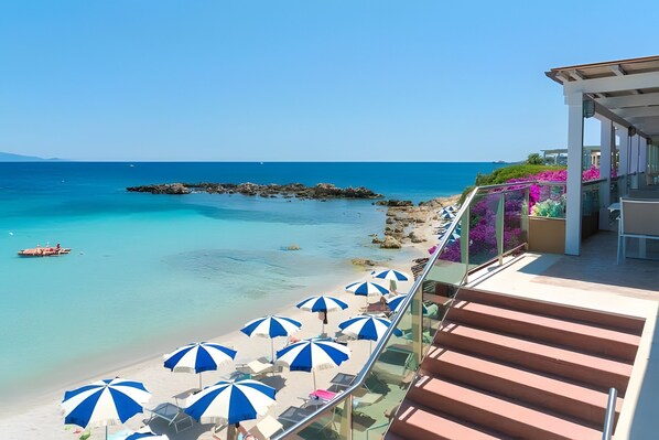 Un balcon avec vue sur une plage, une eau d’un bleu limpide et un promontoire rocheux.