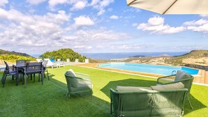 Zona junto a la piscina con sillas, una mesa y vista al mar.
