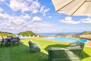 Zona junto a la piscina con sillas, una mesa y vista al mar.