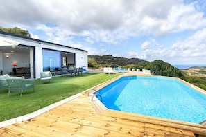Une maison moderne dotée d’une piscine, d’une pelouse verdoyante et offrant une vue sur les collines.