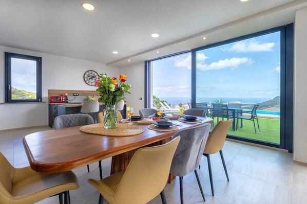 A modern dining area with a wooden table, chairs, and a view of the ocean.