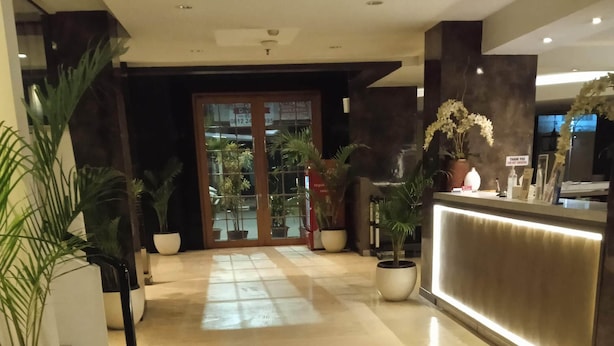 A hotel reception area with a polished marble floor, potted plants, and a reception desk. - La Asiana Express Hotel (Bandung)