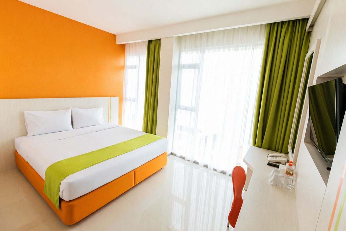 Habitació d'hotel amb un llit, una televisió, un telèfon i una finestra amb cortines.