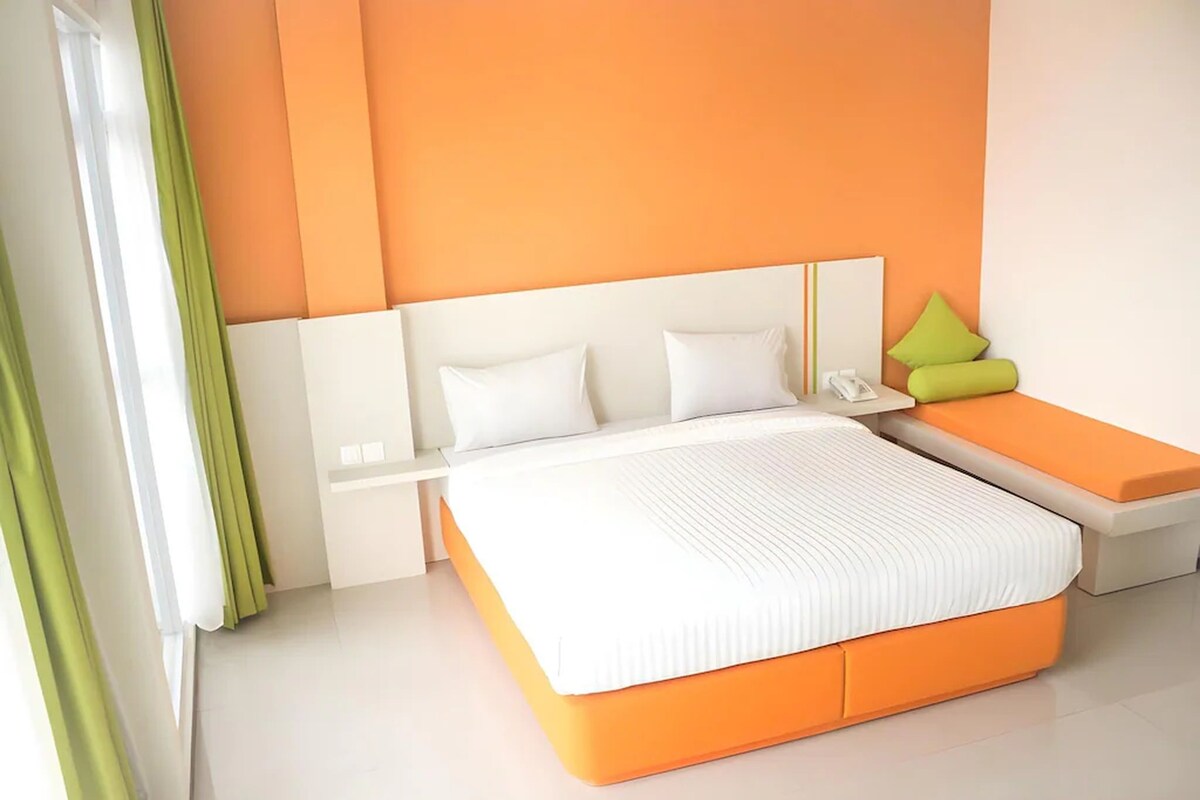 Una habitación de hotel moderna con una cama grande, una mesita de noche y una pequeña zona de estar.