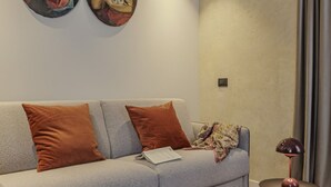 A modern living room with a grey sofa, two brown cushions, a patterned throw, a small round table with a lamp, and two wall-mounted paintings. - ApartmentsArena - Palazzo Cignaroli® - Il Maestro (Verona)