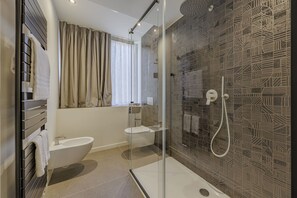 A modern bathroom with a glass shower enclosure, a toilet, and a bidet.