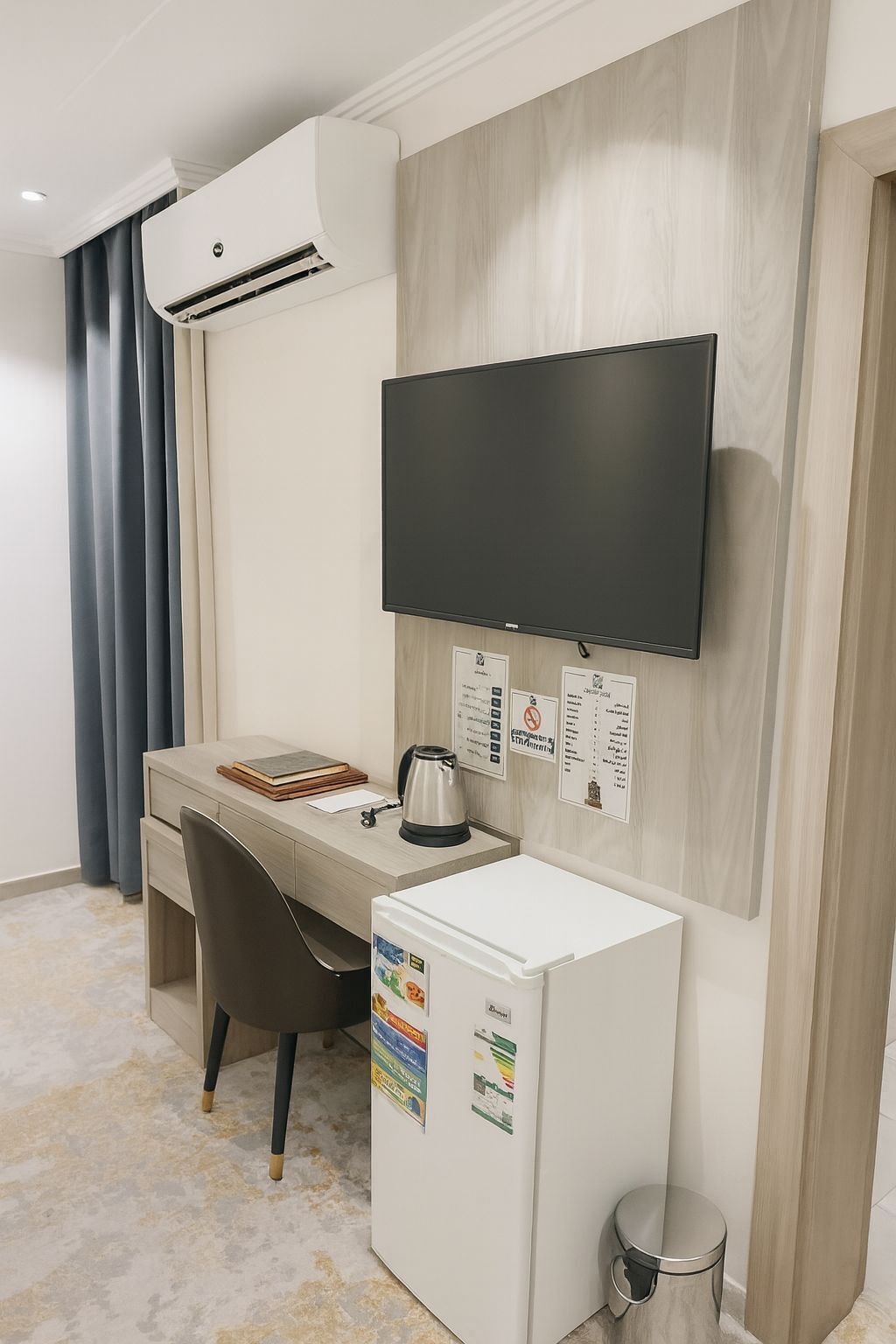 Habitación de hotel con escritorio, silla, televisión de pantalla plana, equipo de aire acondicionado y refrigerador.