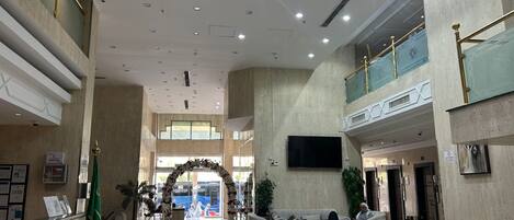 A spacious lobby with a high ceiling, a reception desk, seating areas, and a large screen.