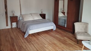 A bedroom with a wooden floor, a bed with a grey bedspread, two bedside tables with lamps, a wooden wardrobe, and a chair. - Le Balcon d'Arcyate (Arcy-sur-Cure)