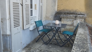 A small outdoor seating area with a table and chairs, a window with shutters, and a stone wall. - Le Balcon d'Arcyate (Arcy-sur-Cure)