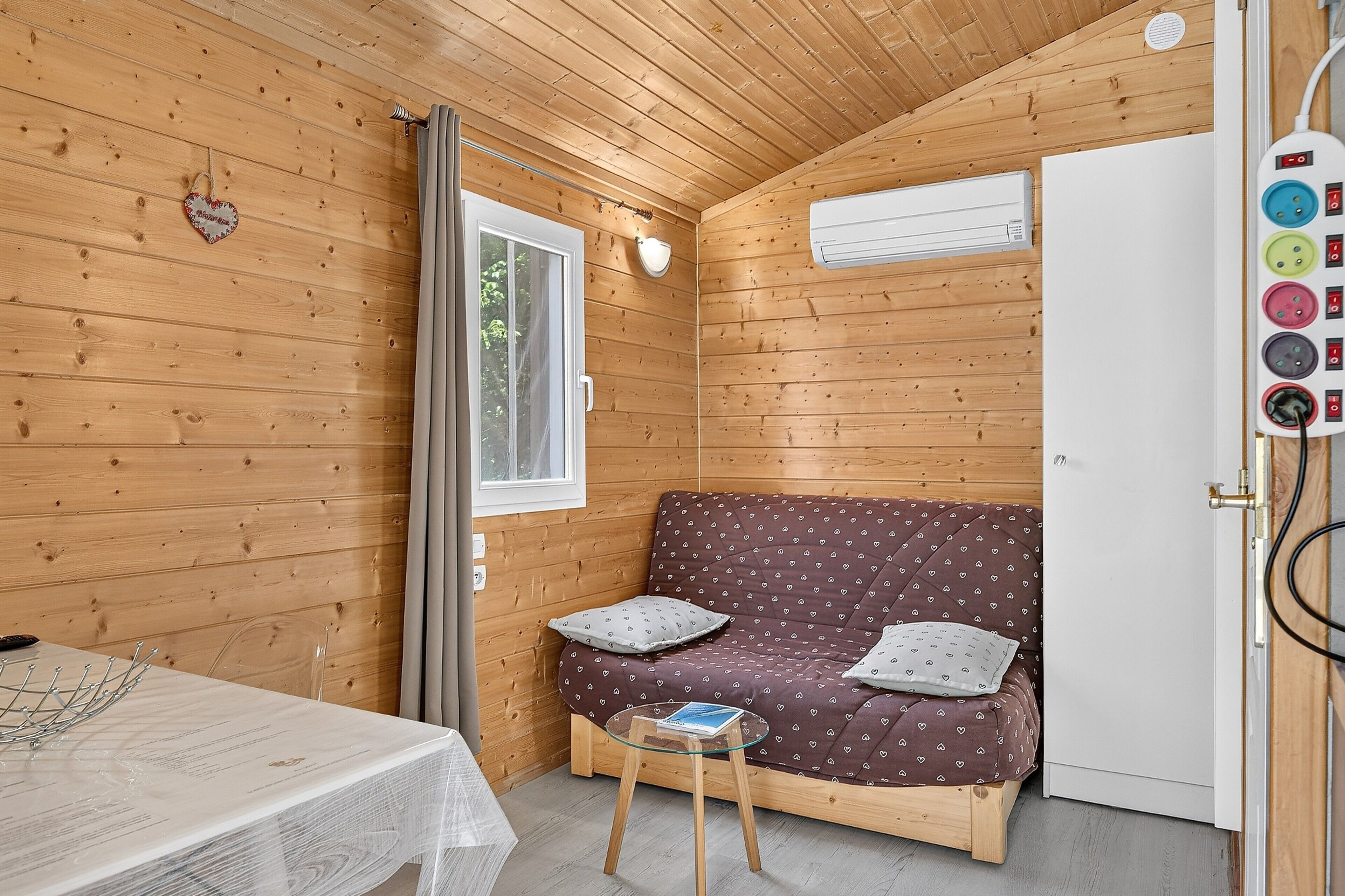 L’intérieur d’un chalet en bois, avec un canapé, une table et une porte dotée d’une prise de courant.