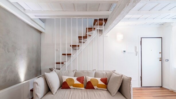 Een moderne woonkamer met een beige bank, een houten trap en een witte deur.