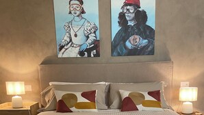 Een tweepersoonsbed met gestreept beddengoed, twee wandlampen en twee kunstwerken in lijsten erboven.