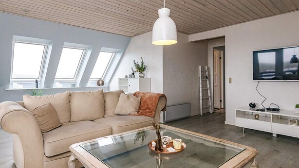 Ein modernes Wohnzimmer mit einem beigen Sofa, einem Glastisch und einer weißen TV-Konsole.