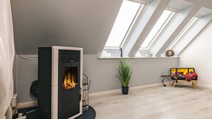 Ein modernes Schlafzimmer im Loft-Stil mit Kaminofen, Dachfenstern, einer Topfpflanze und einem Bett mit roter Decke.