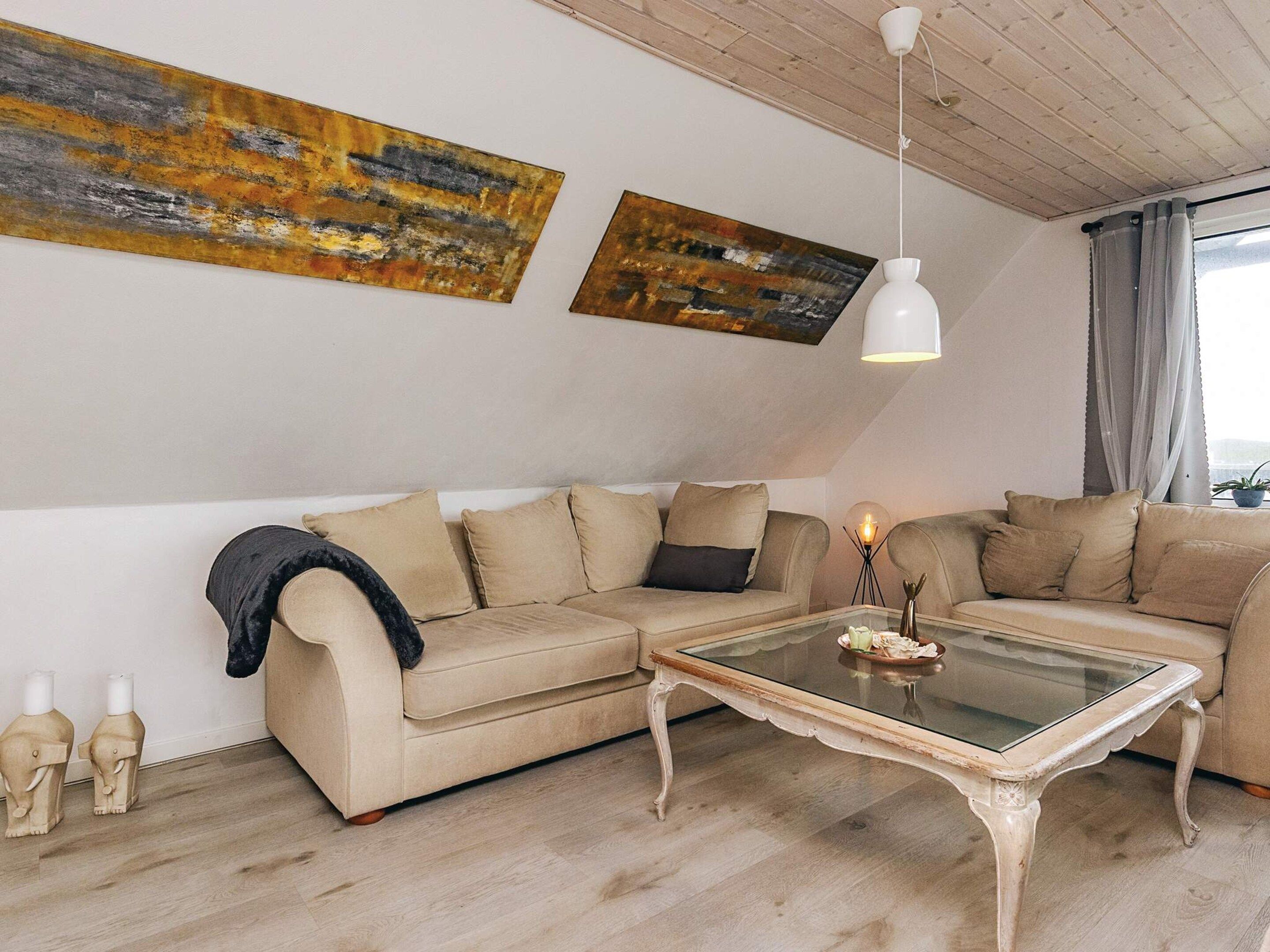 A modern living room with a sectional sofa, a glass coffee table, and two abstract paintings on the wall.