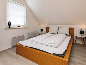 A modern bedroom with a wooden bed frame, a radiator, a window with blinds, and bedside tables with lamps.