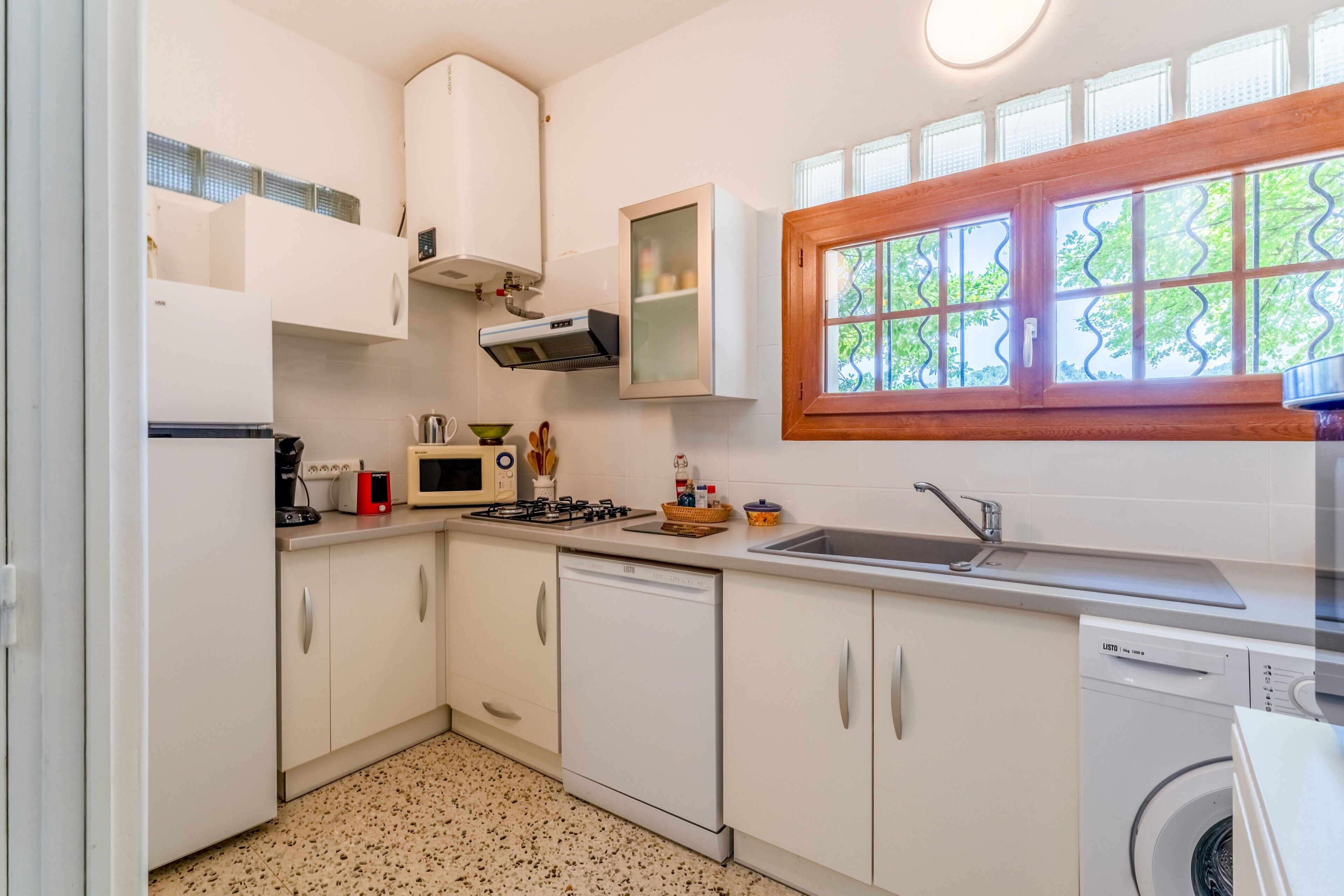 A compact kitchen with white cabinets, a microwave, a stove, a sink, and a washing machine.