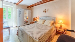 A bedroom with a bed, a nightstand, a lamp, a wardrobe, and a bench. - 'Chez Martha' with Mountain View, Private Terrace and Garden (Anduze)