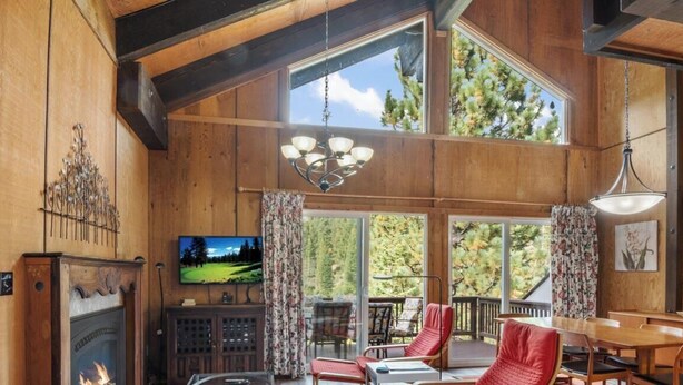 A spacious living room with a fireplace, a television, and a large window overlooking a deck.