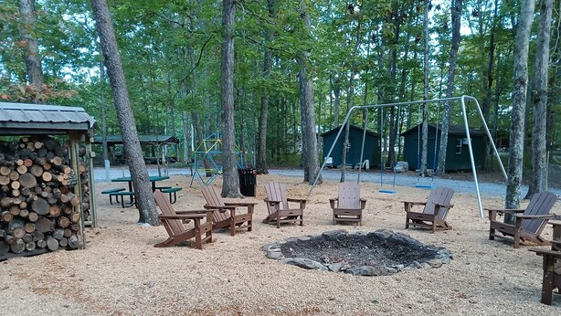 A campground with wooden chairs, a fire pit, and a swing set.