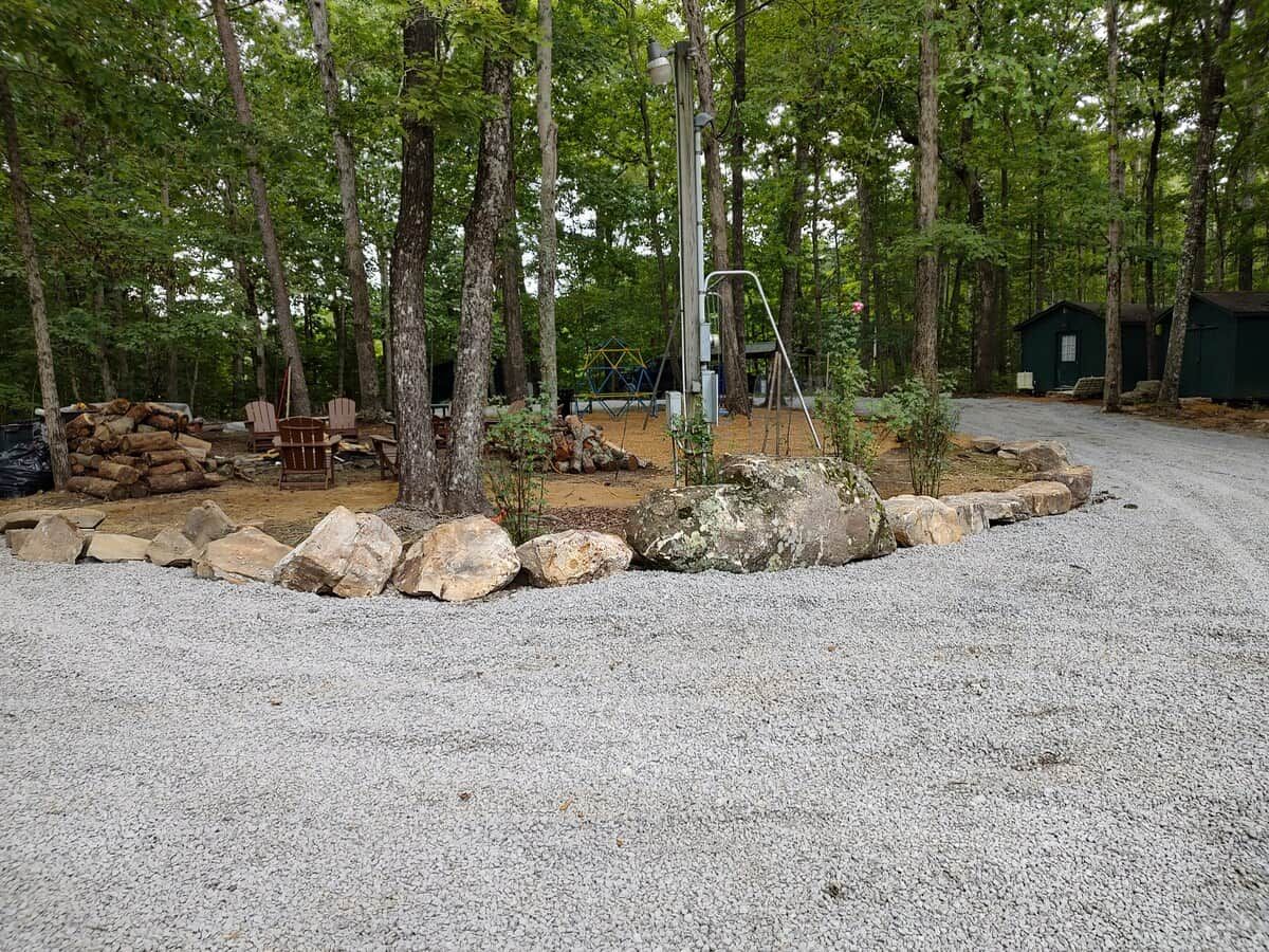 A gravel parking area with a wooden fence, trees, and a playground.