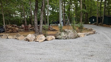 A gravel parking area with a wooden fence, trees, and a playground.