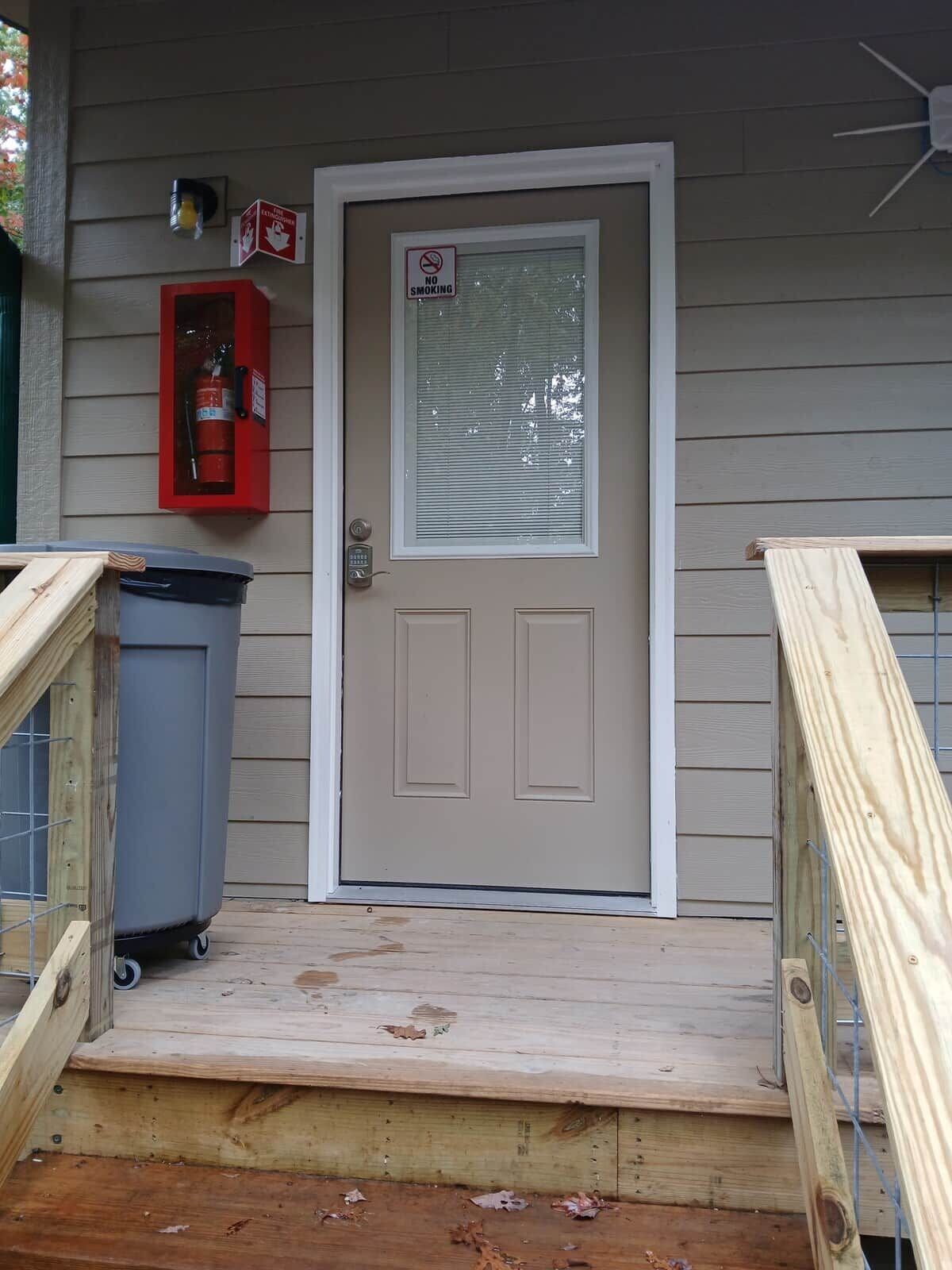 Puerta principal con un cartel de 'No Fumar', un extintor y un buzón.