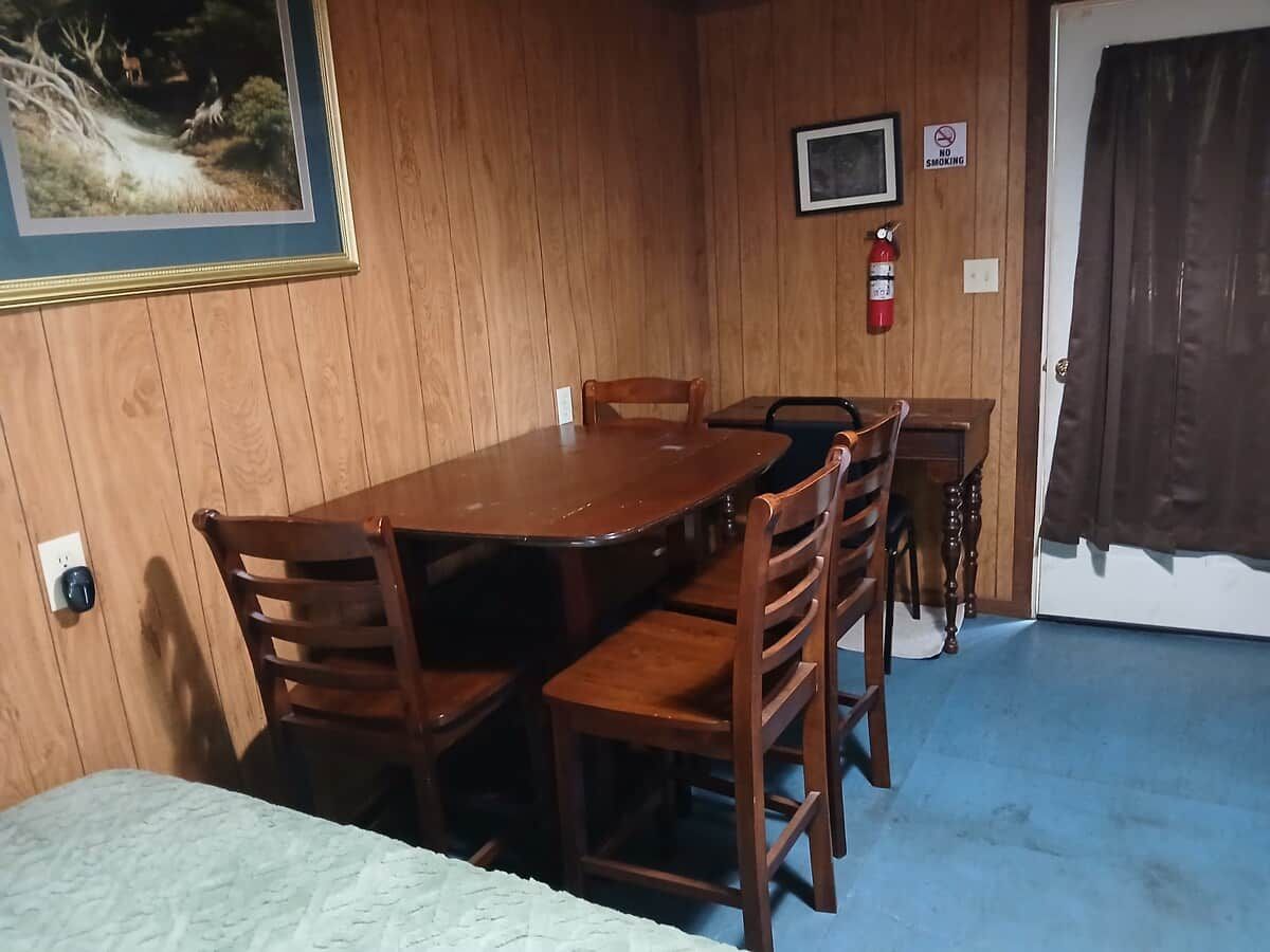A room with a wooden dining table and chairs, a television, a fire extinguisher, and a door with a curtain.