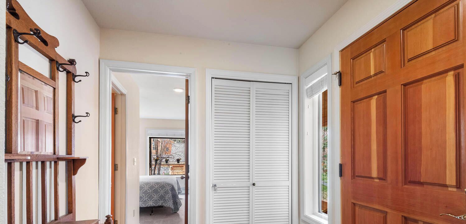 Un couloir avec des portes en bois, un lit recouvert d’une couvre-lit à motifs et une vue sur une autre pièce.
