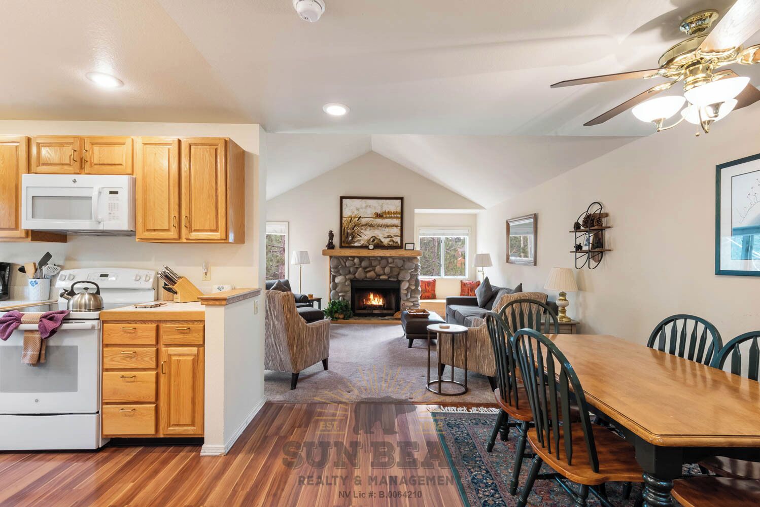 A kitchen with wooden cabinets, a microwave, and a stove. There is a dining area with a table and chairs, and a fireplace in the background.