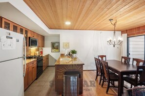 Cozinha com armários de madeira, fogão embutido e área de refeições com mesa e cadeiras.