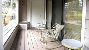 A covered porch with two rocking chairs and a small table, a door, and a window with blinds.