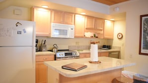 A kitchen with wooden cabinets, a white refrigerator, a microwave, and a coffee maker. There is a small island with stools and a book.