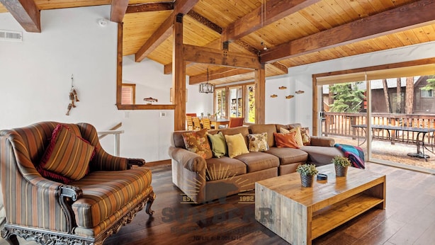 A spacious living room with a high ceiling, wooden beams, a large sofa set, a coffee table, and a view of the outdoors.