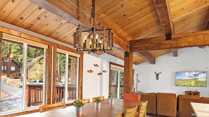 A spacious room with large windows, a wooden ceiling, a dining area with a table and chairs, and a mounted television.