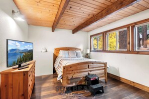 A bedroom with a wooden bed, a TV on a wooden dresser, a window with a view of trees, and a wooden ceiling. - 3 Bedroom Open Space Condo (IC3-72) (Incline Village)