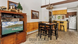 Ein Wohnzimmer mit Fernseher, Holzmöbeln, einem Essbereich und einer Küche mit Holzausstattung und Kühlschrank.