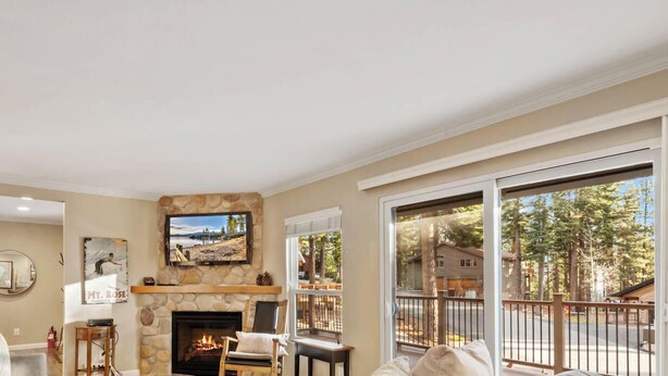 A living room with a stone fireplace, a mounted TV, and a large window overlooking a residential area.