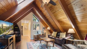 A cozy loft-style room with a wooden ceiling, a fireplace, a leather sofa, and a television.