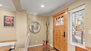 A room with a wooden door, a round mirror, a dining table with chairs, and a window with blinds.