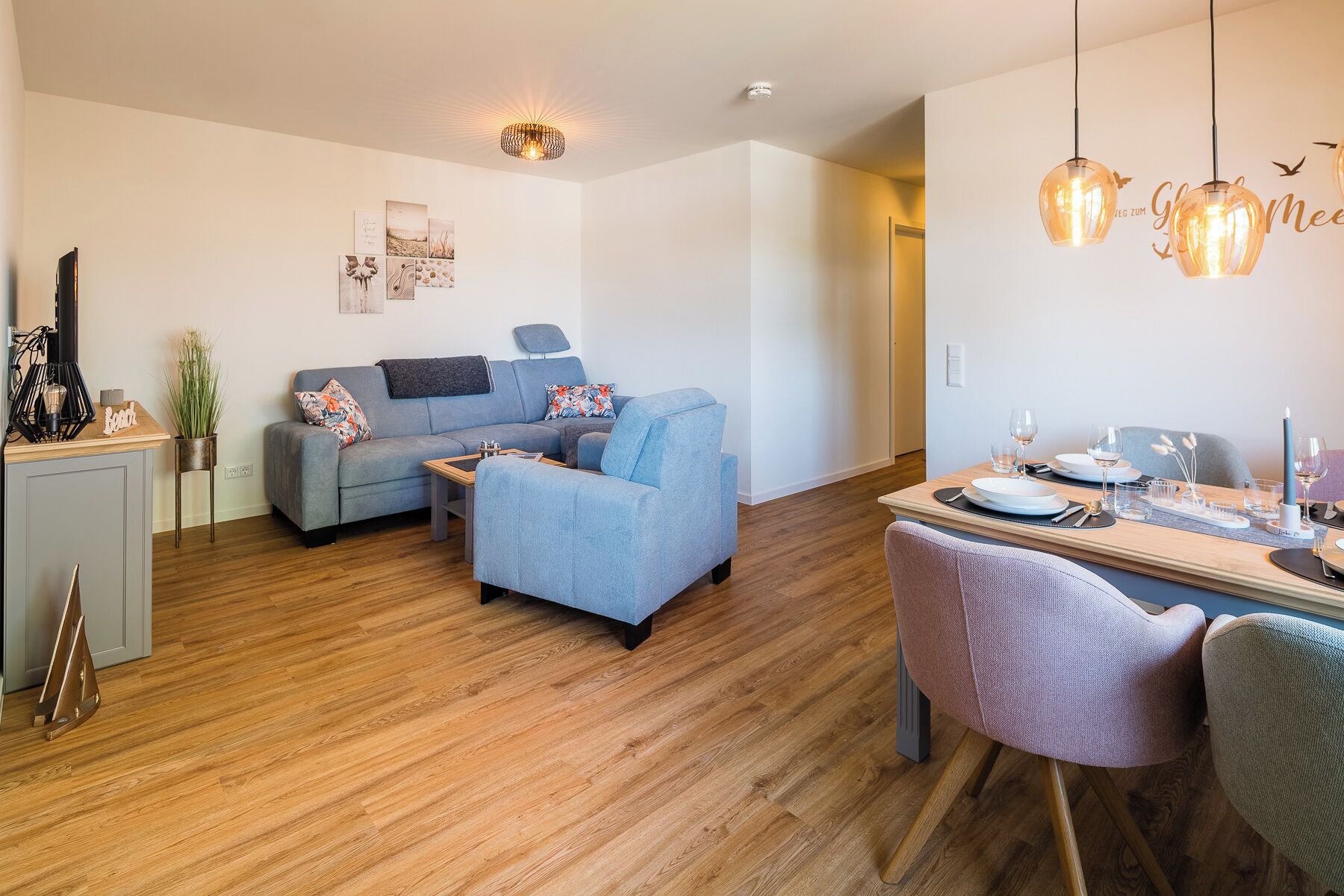 A modern living room with a grey sofa, a small table, and a dining area with a table set for two.