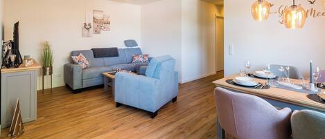 A modern living room with a grey sofa, a small table, and a dining area with a table set for two.