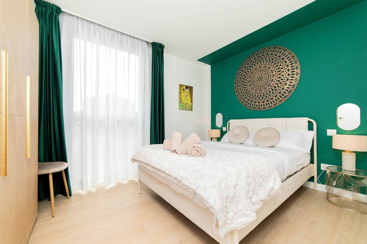 A modern bedroom with a bed, a chair, and a decorative wall piece.