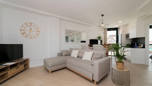 A modern living room with a sectional sofa, a flat-screen TV, a wall clock, and a potted plant.