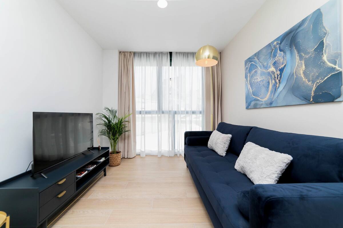 A modern living room with a dark blue sofa, a flat-screen TV, a large abstract painting, and a potted plant.