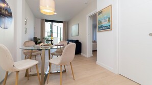 A modern living room with a glass dining table, comfortable seating, a hanging light fixture, and a cityscape poster on the wall.