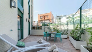 A small outdoor patio with white lounge chairs, a table, and chairs.