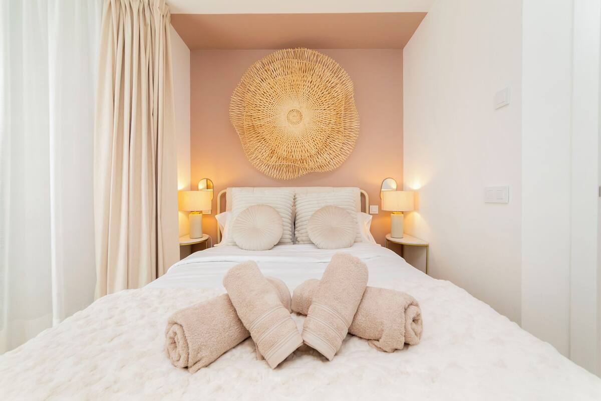 A neatly made bed with rolled towels, a circular wall decoration, and two bedside lamps.