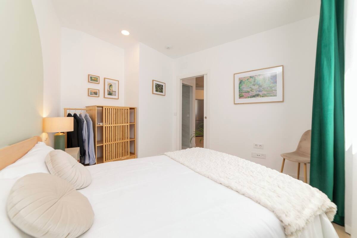 A bedroom with a bed, a wardrobe, a chair, and a door leading to another room.